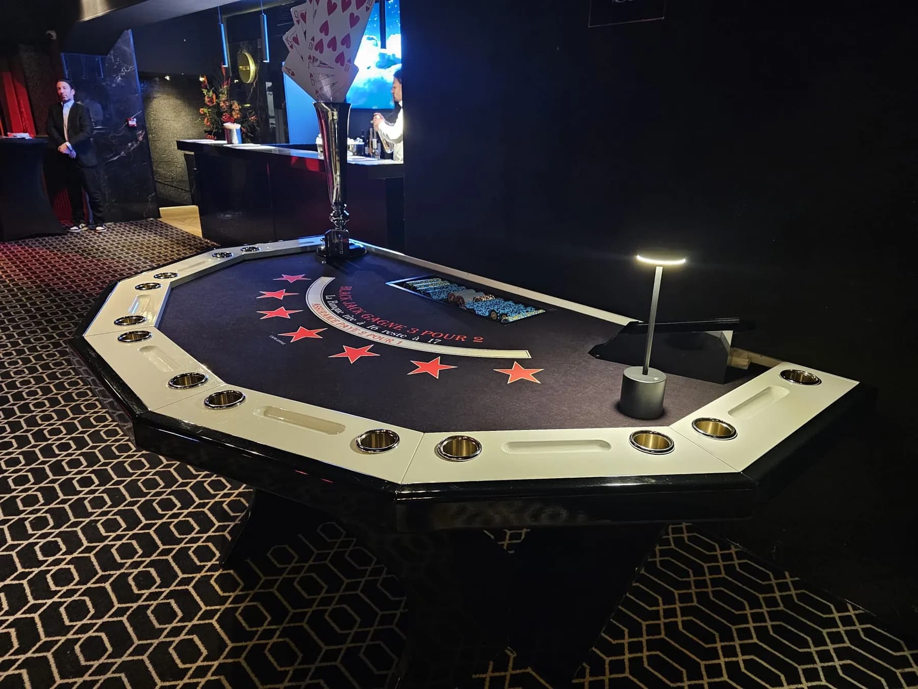 Table de blackjack octogonale blanche sur un sol à motifs dorés, dans une salle sombre