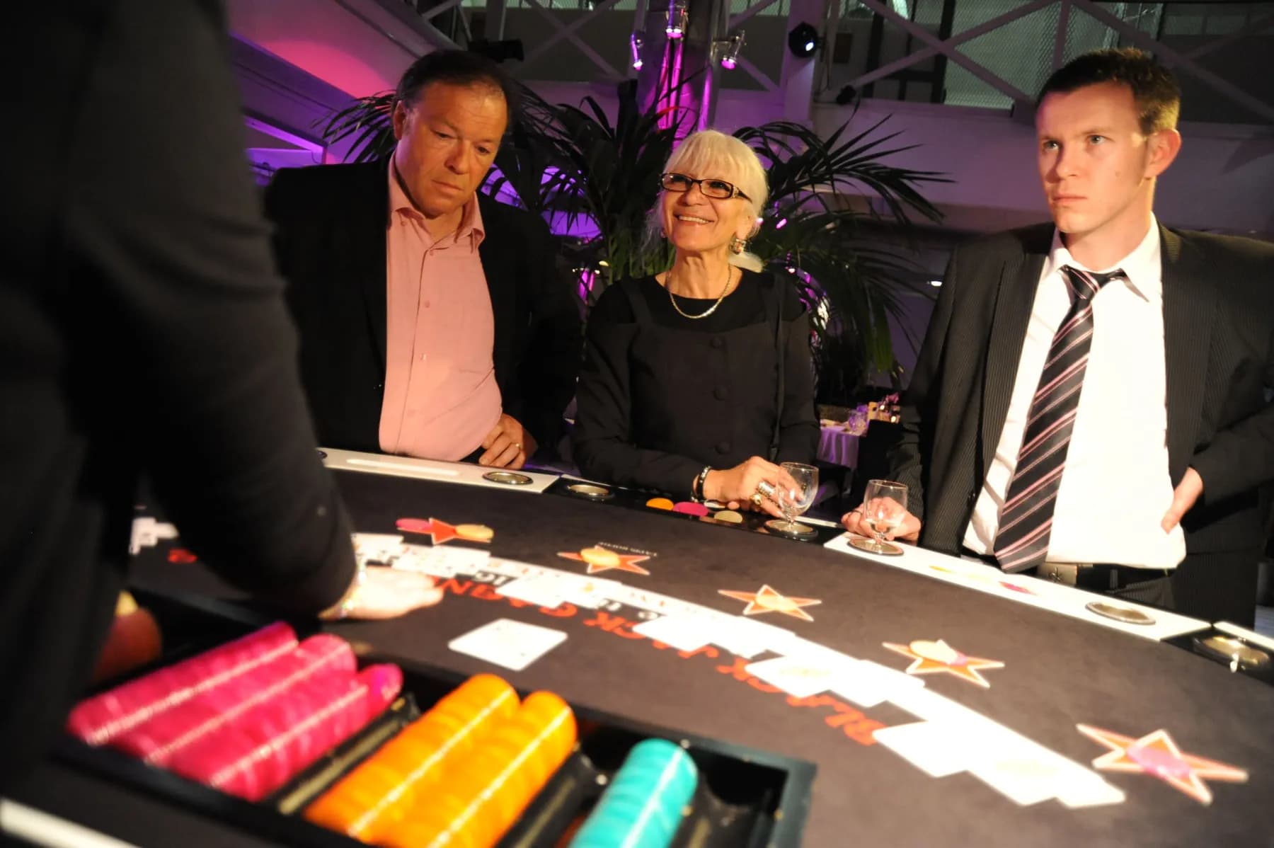 Trois invités accoudés à une table de blackjack, jetons colorés au premier plan