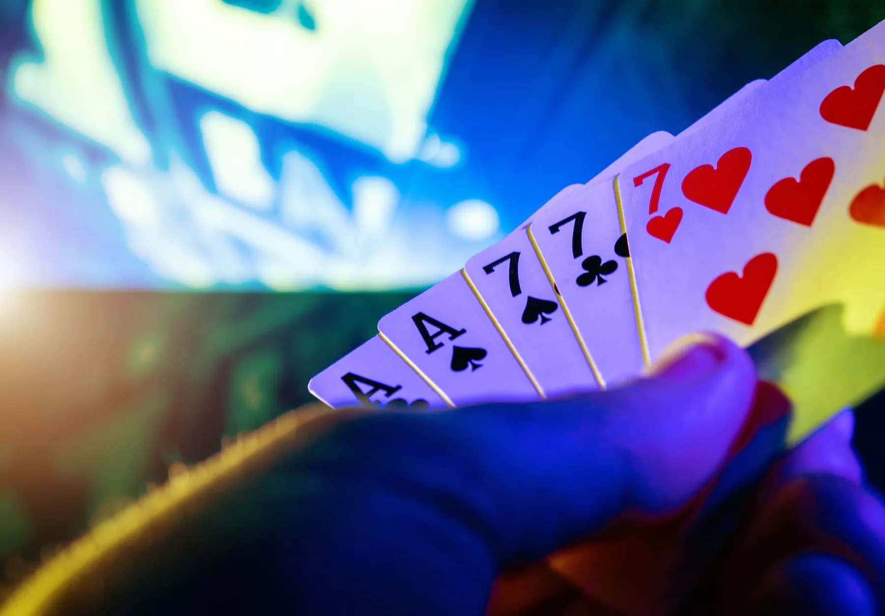 Une main tient un éventail de cartes de poker sous des lumières de néon