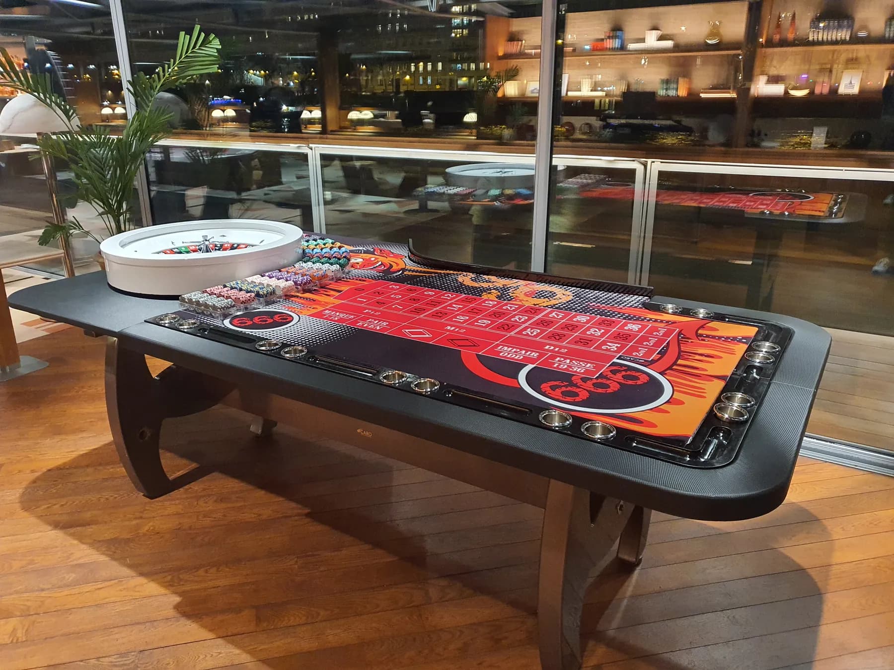 Table de roulette anglaise sur un parquet, baies vitrées de nuit en arrière-plan