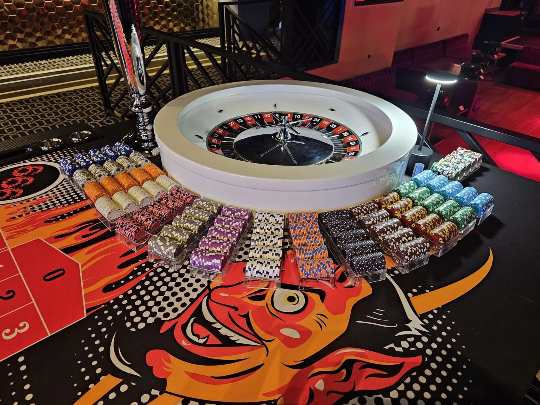 Cuvette blanche de roulette entourée de piles de jetons, sur un tapis illustré d’un diable